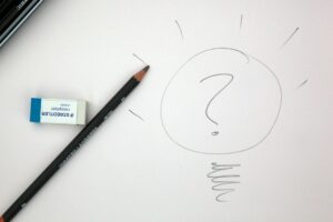 A lead pencil and an eraser on a white page with a question mark drawn on it in pencil.
