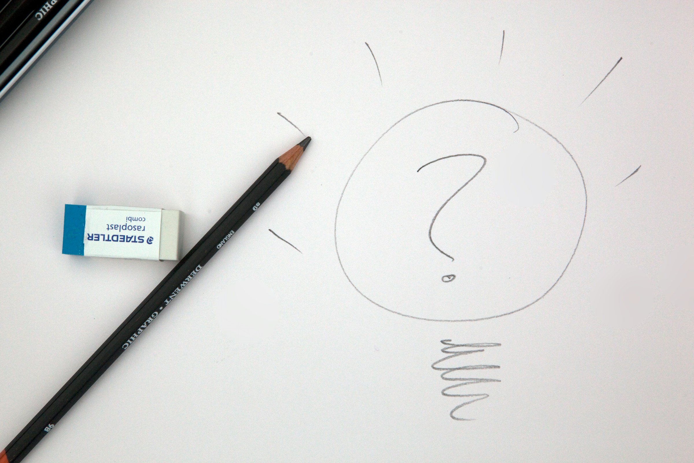 A lead pencil and an eraser on a white page with a question mark drawn on it in pencil.