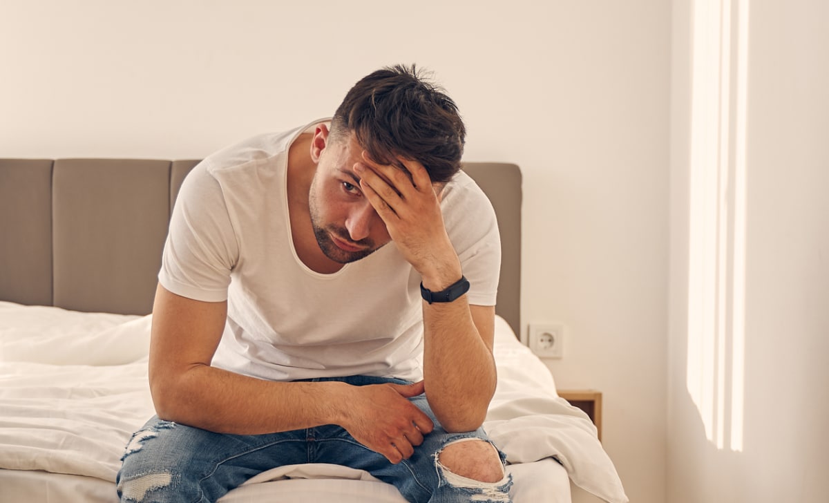 Anxious Caucasian man spending time at home in the bedroom while thinking of his problems.