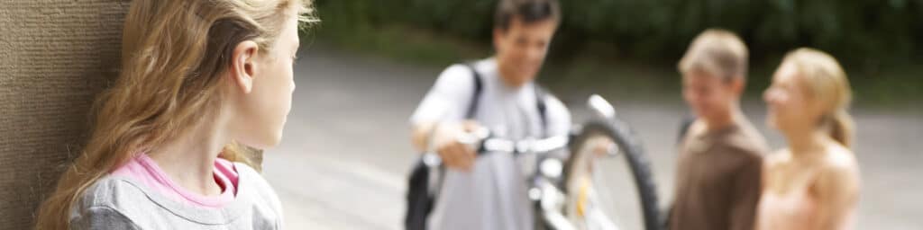 A pensive teenager with other teens and a bicycle in the background.
