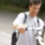 A pensive teenager with other teens and a bicycle in the background.