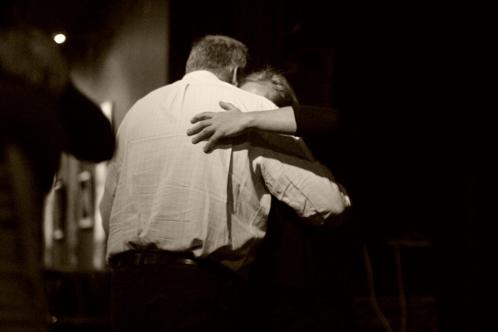 Two people embrace in a dimly lit room